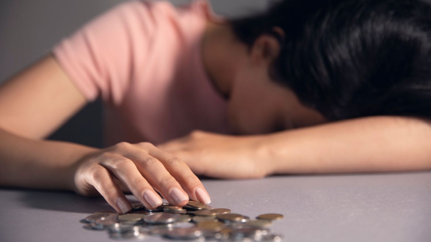 Verzweifelte Person mit Kopf auf dem Tisch und Euro-Münzen, symbolisiert Armut und Schulden.