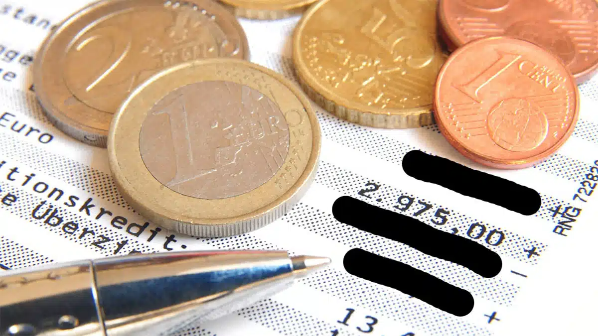 Münzen und Kugelschreiber auf Kontoauszug mit geschwärzten Passagen