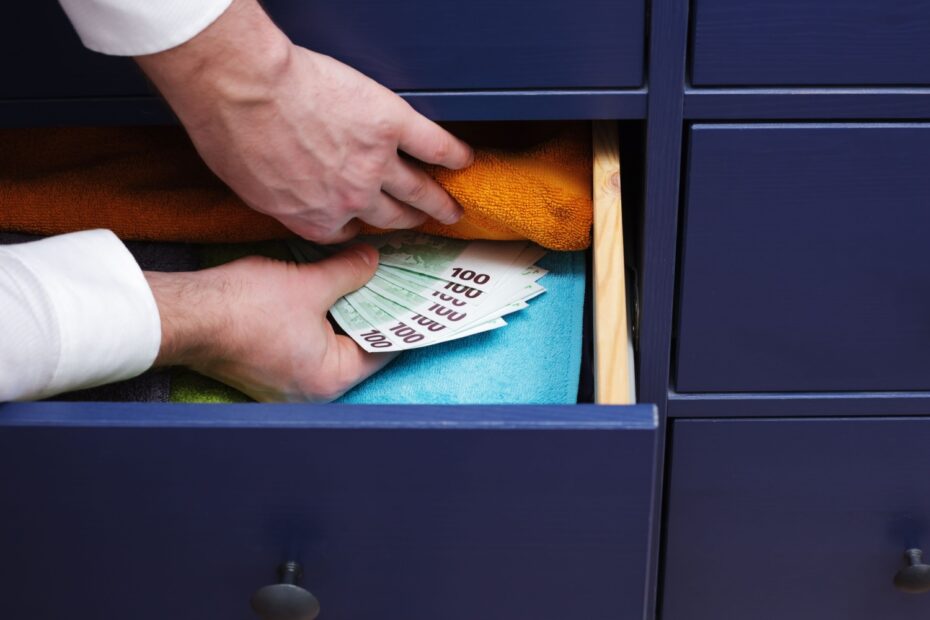 Hände verstecken Geldscheine zwischen Handtüchern im Schrank