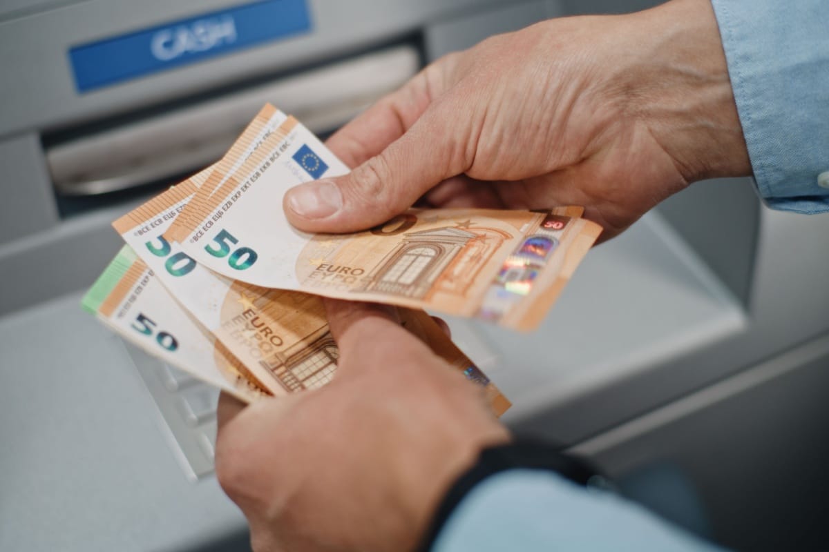 Hände zählen Geldscheine am Automaten, symbolisch für Bürgergeld-Höhe des Jobcenters