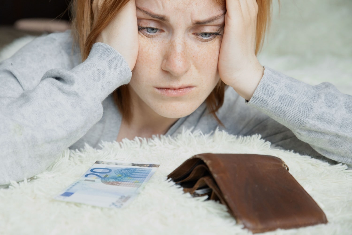 Junge Frau sitzt besorgt vor leerem Geldbeutel und einem 20-Euro-Schein – Symbol für finanzielle Not und zu geringe Bürgergeld-Zahlungen.