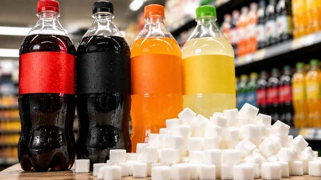 Flaschen mit Cola und Limonade stehen im Supermarkt neben einem großen Haufen Zuckerwürfel.